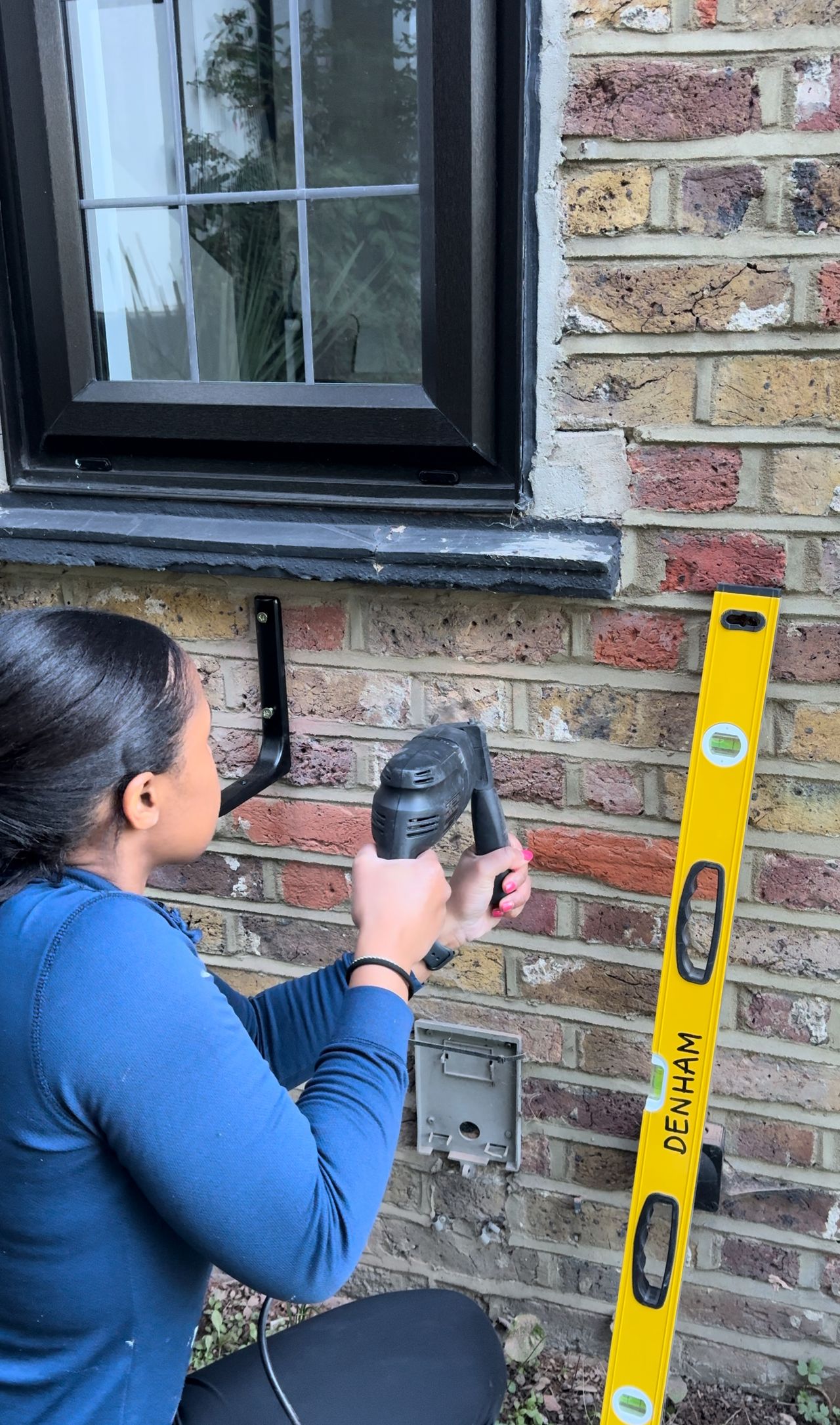 A woman drilling into an exterior brick wall wearing PPE to protect her eyes