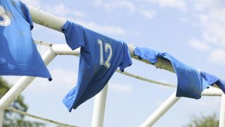 Blue soccer jerseys hanging on the post of a soccer goal with dirt on them.
