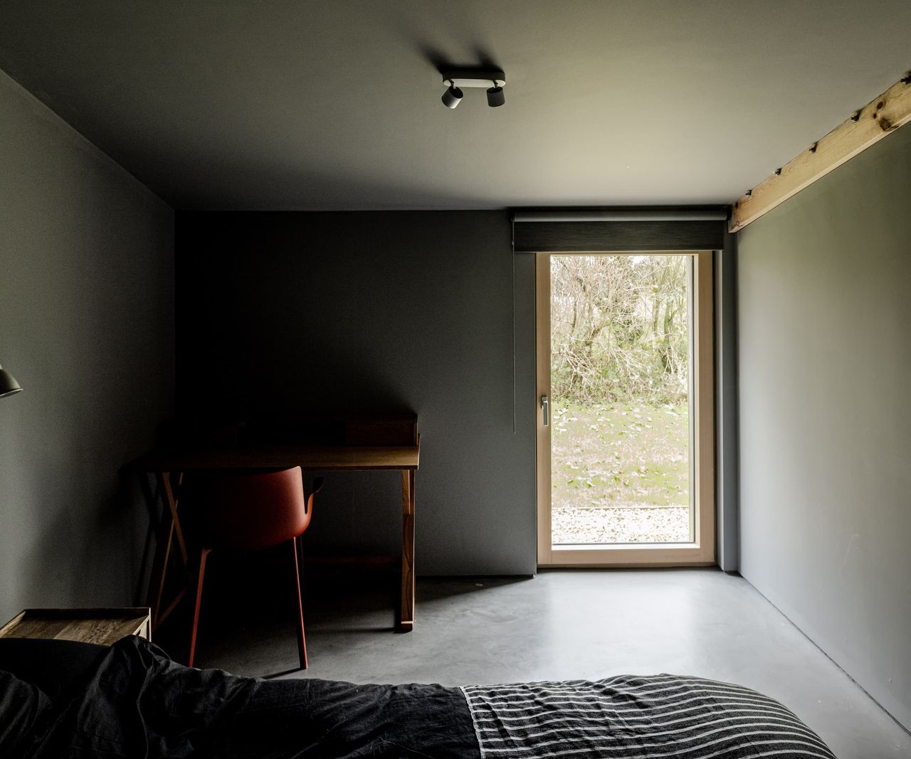 A black bedroom with a side table made from wood and a door illuminating the room