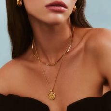 A woman wearing matching gold necklaces and thick gold earrings from Missoma.