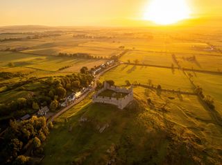 Sunset behind Hume Castle from a drone very yellow-orange view