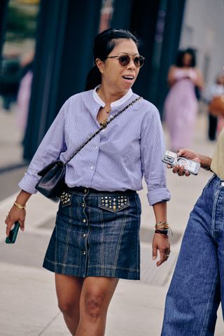 A NYFW SS25 Street Style guest wearing a blue button down and denim mini skirt