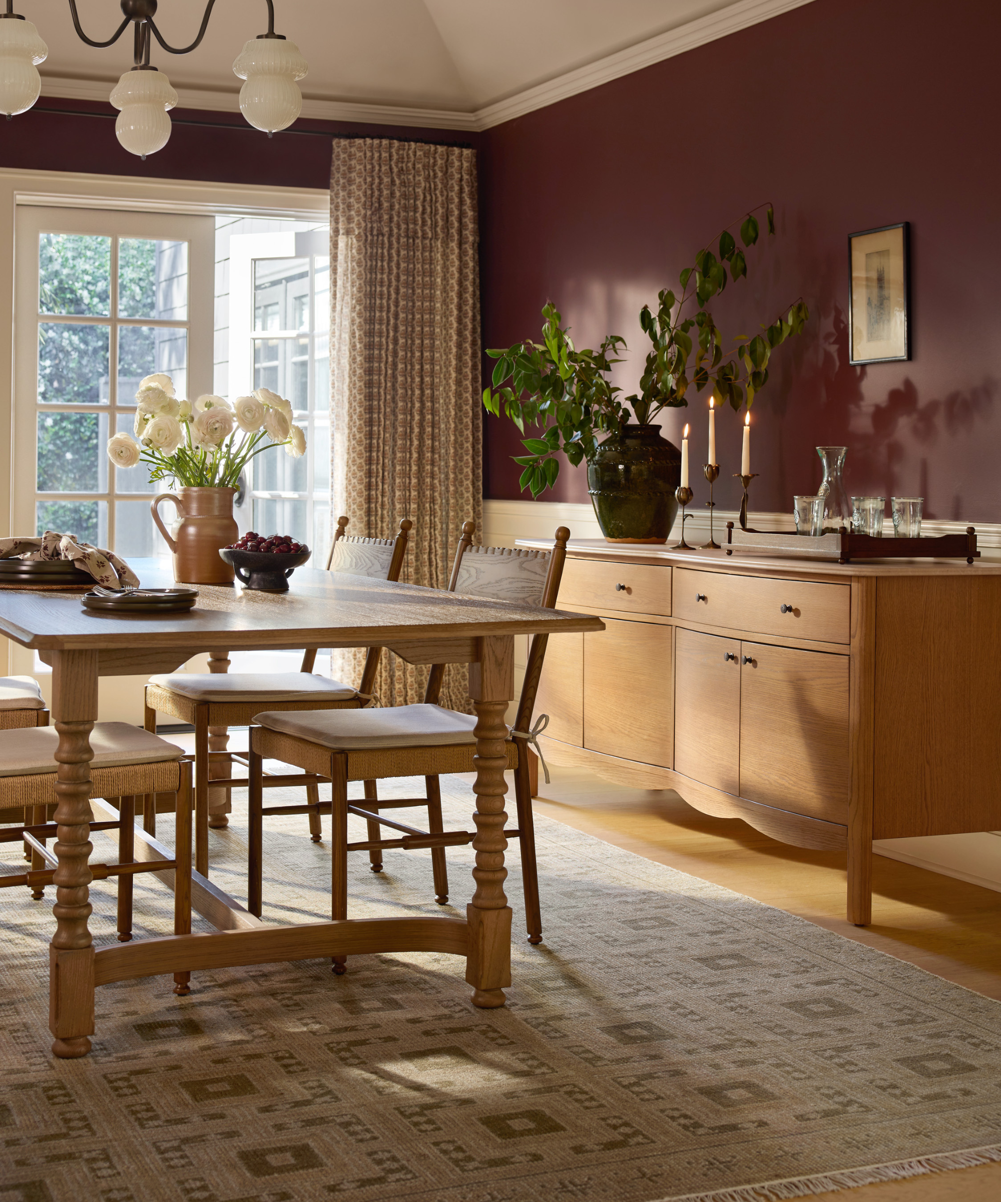 a cozy dining room with a light wood table, chairs, a credenza, and maroon painted walls