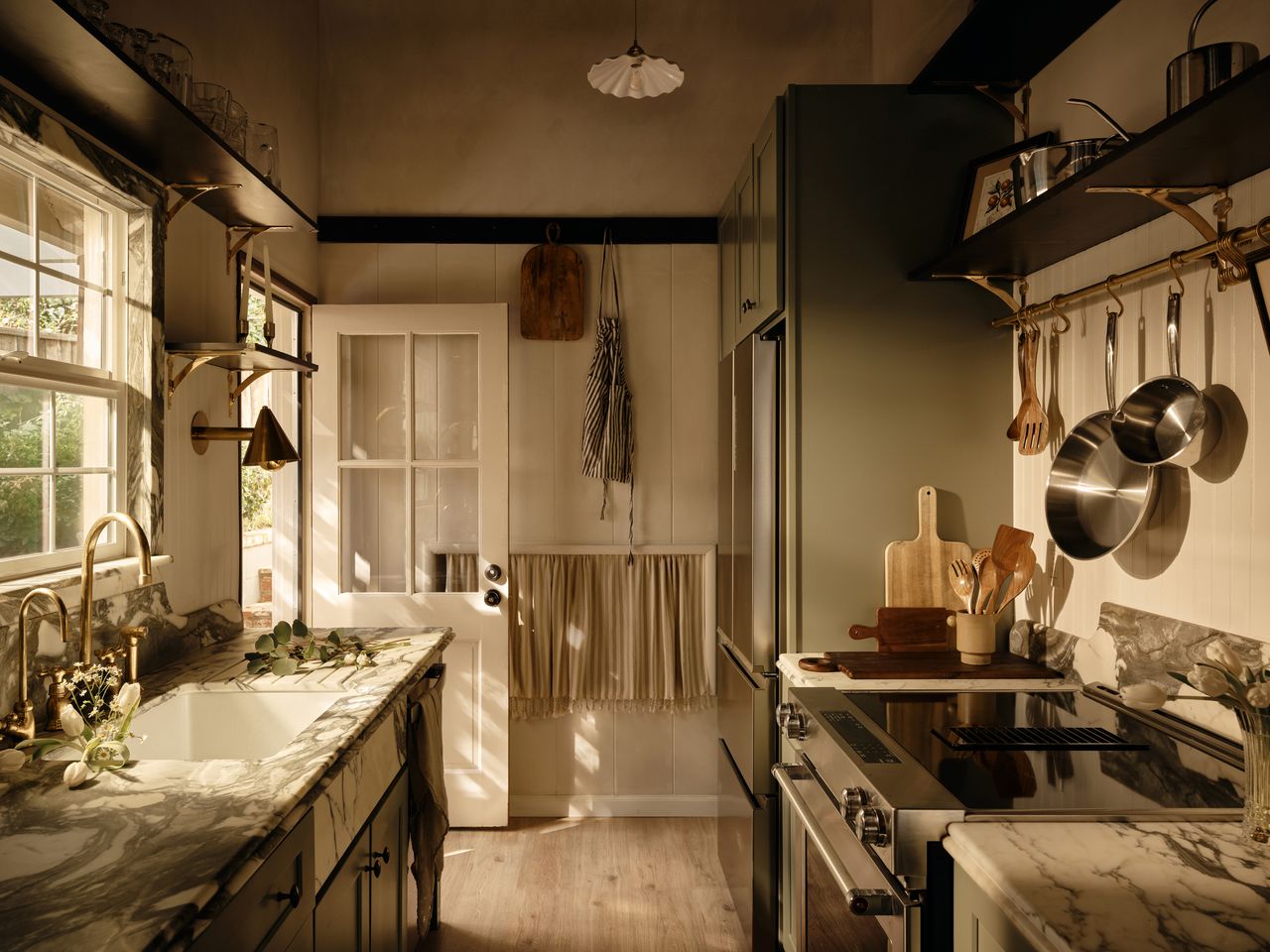 A rustic galley kitchen with marble countertops, wooden flooring, and sage green cabinetry 