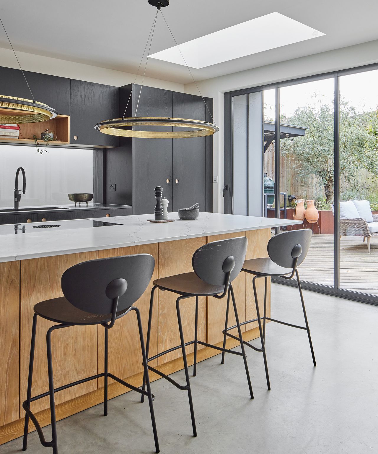 A contemporary kitchen with large central island with bar stools. There are low hanging pendant lights over the island