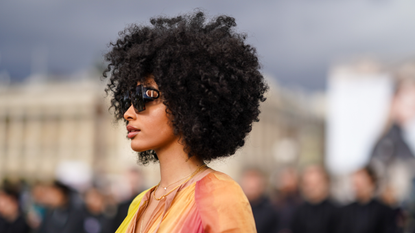 A guest wears Dior sunglasss, a yellow and pink pleated dress, outside Dior, during Paris Fashion Week - Womenswear Fall/Winter 2020/2021, on February 25, 2020 in Paris, France.