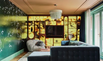 Living area with backlit cabinetry, green mural wall, teal corner sofa and pale grey armchair