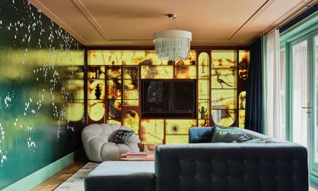 Living area with backlit cabinetry, green mural wall, teal corner sofa and pale grey armchair