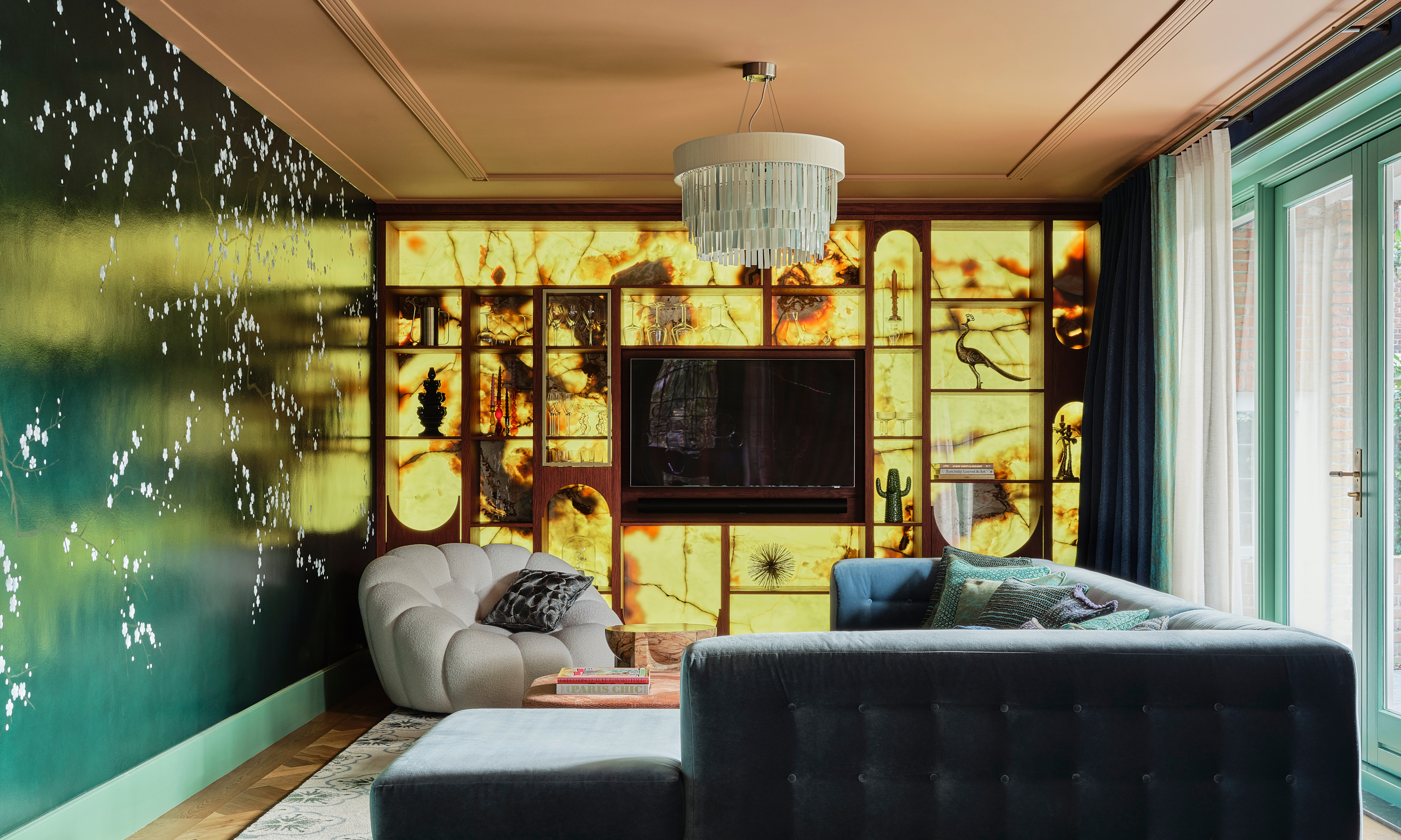 Living area with backlit cabinetry, green mural wall, teal corner sofa and pale grey armchair