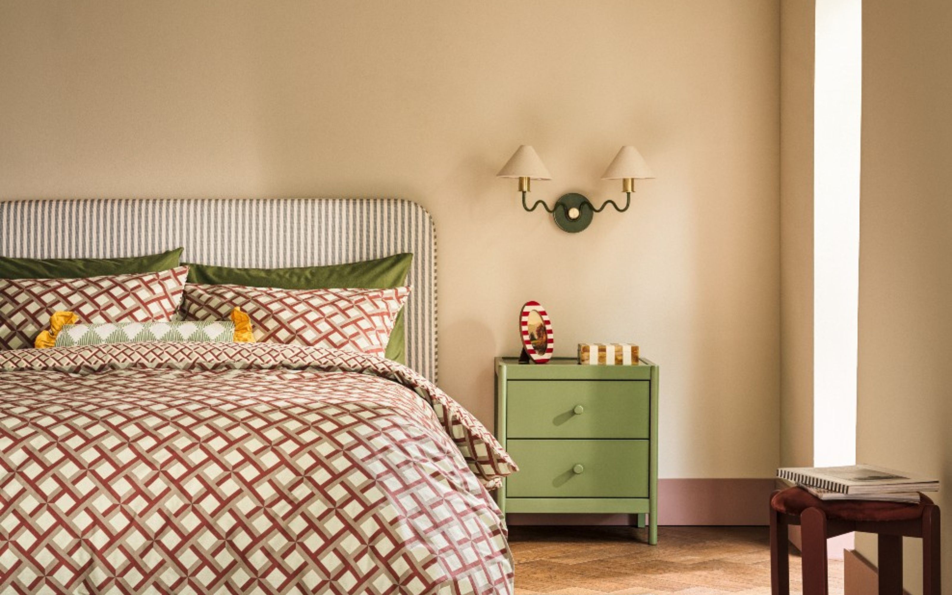 Habitat Wiggle Metal 2 Light Wall Light - Green &amp; Natural, hanging above green bedside table on beige wall with green striped headboard and red patterned bedding