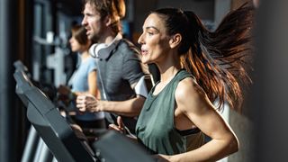 Woman running on a treadmill, man running on the next treadmill in the background