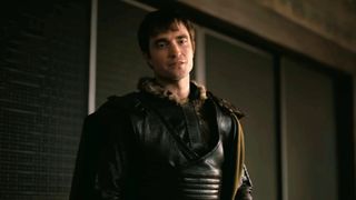 A screen shot of Robert Pattinson as Antinous looking serious while wearing black leather.
