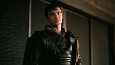 A screen shot of Robert Pattinson as Antinous looking serious while wearing black leather.
