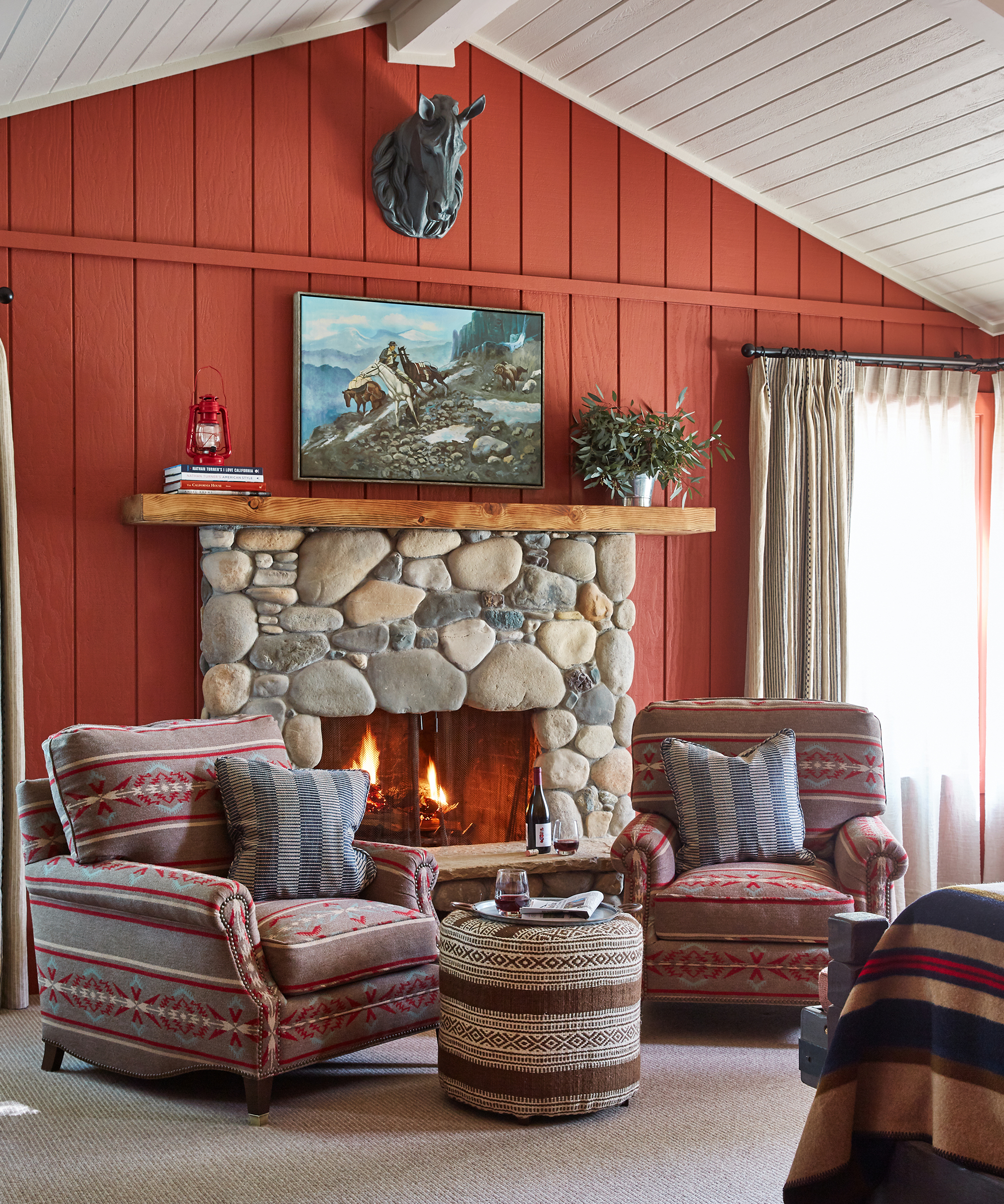 two armchairs in front of a stone fireplace and red painted wood clad wall