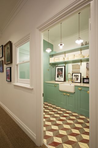 A stylish utility room with mosaic tiled flooring, green cupboards and an internal window for extra light