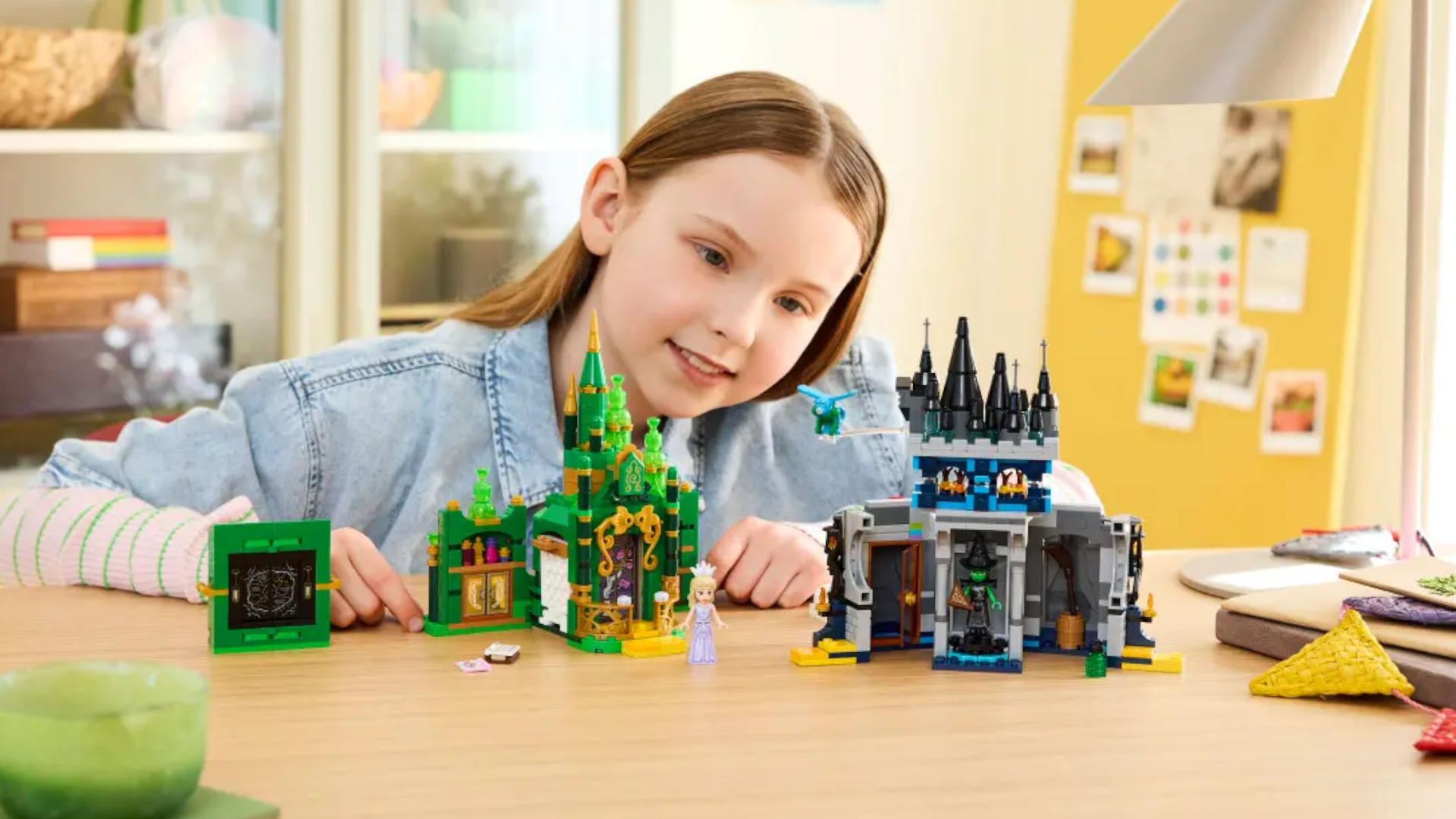 A smiling girl at a table looks at and plays with the Lego Emerald City &amp;amp; Kiamo Ko Castle set