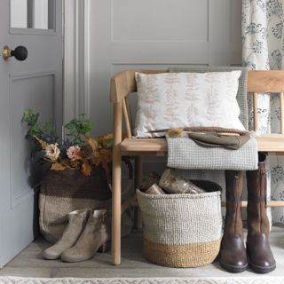 A grey panelled hallway with a wooden bench with fabric storage baskets placed under and next to it