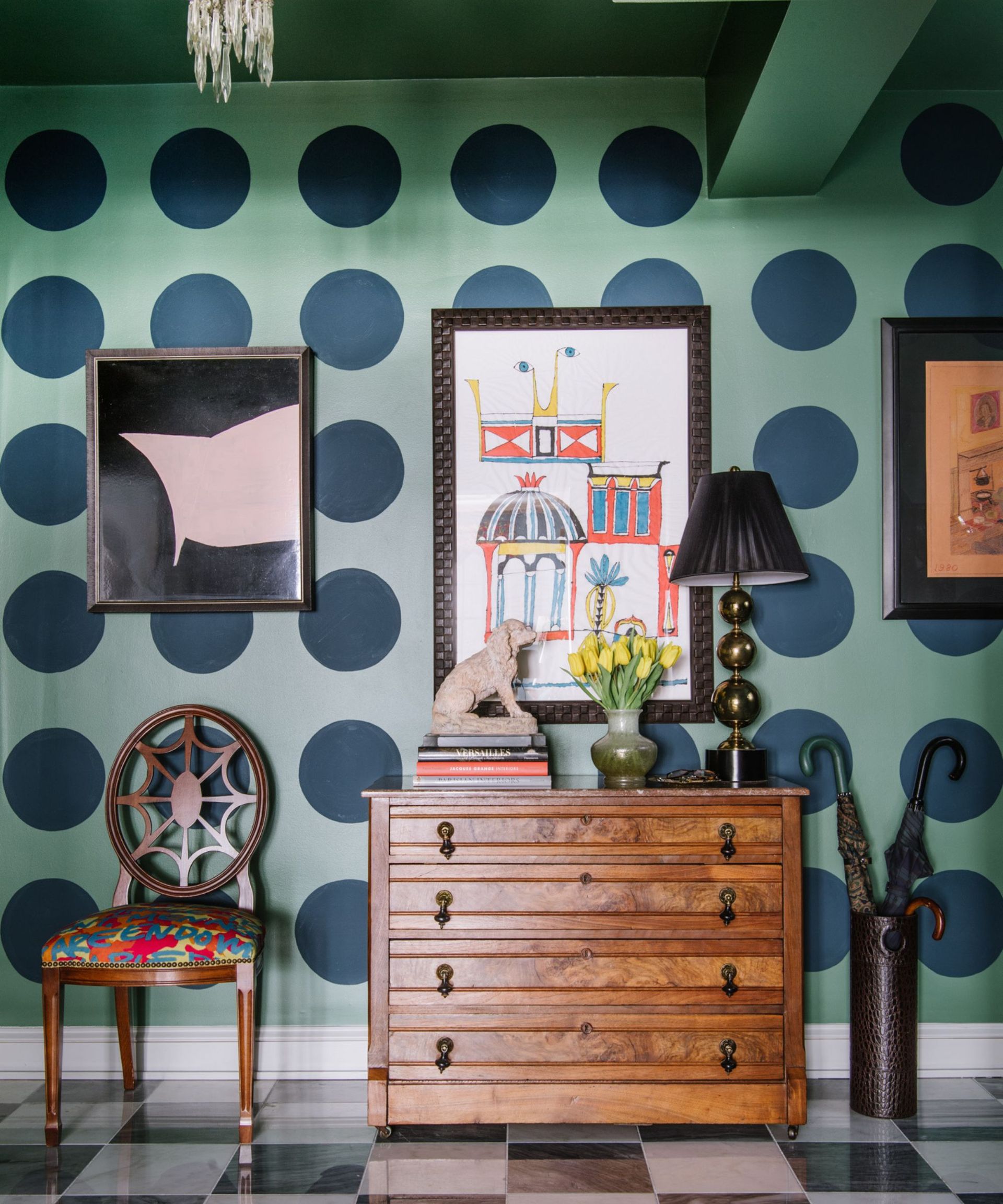 Hallway with chequered floor and polka dot painted walls, and wood chest of drawers, art work and antique chair