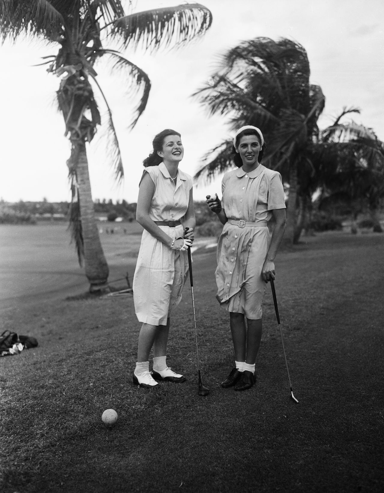 Black and white photograph of two women in belted shirt dresses playing golf