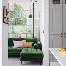 White and grey open-plan living room with corner green velvet sofa in front of a window-style botanical wall mural