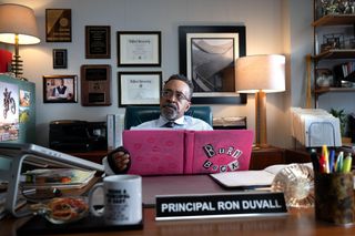Tim Meadows as Principal Duvall sits behind his desk with the pink-covered Burn Book in Mean Girls.
