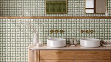A wooden bathroom vanity with dual sinks, against a green tiled wall. 
