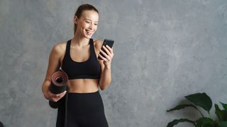 Woman holding a yoga mat during workout holding a smartphone in her left hand