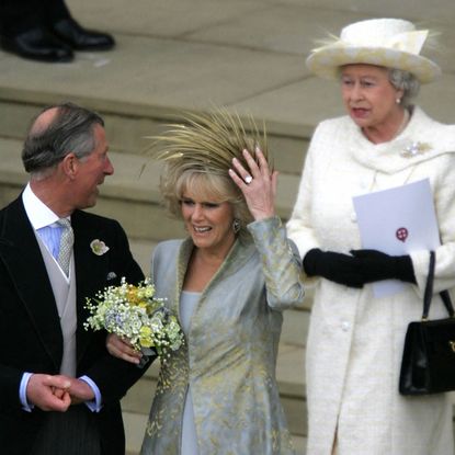 King Charles linking arms with Queen Camilla, holding on to her hat on her wedding day, with Queen Elizabeth standing behind her