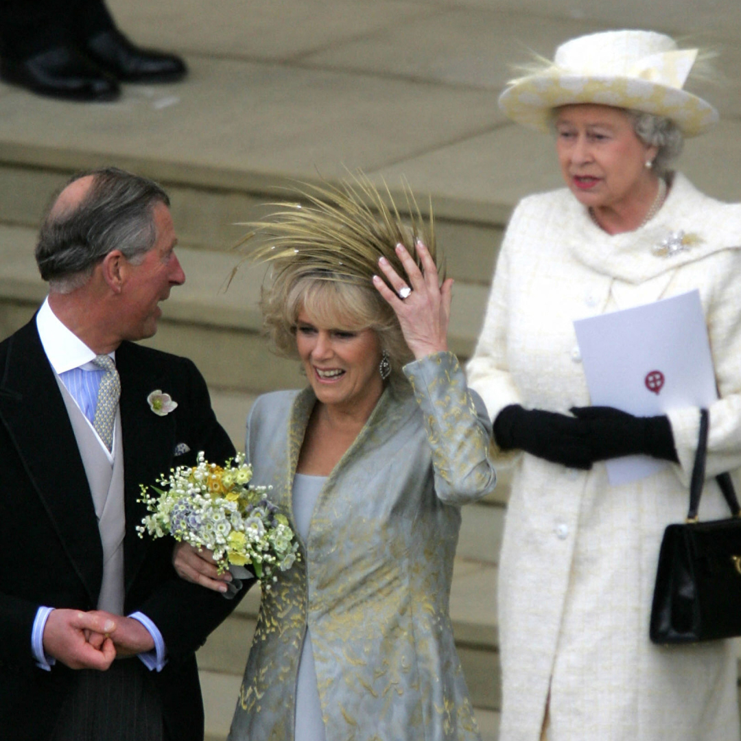 King Charles linking arms with Queen Camilla, holding on to her hat on her wedding day, with Queen Elizabeth standing behind her
