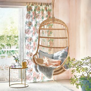 Pink room with hanging wicker chair next to open french doors dressed with floral curtain