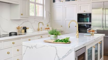 A white kitchen with white marble countertops, double ovens built into units