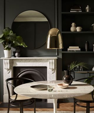 dining room with black walls, a white marble fire place and matching round dining table, and a metallic gold pendant light