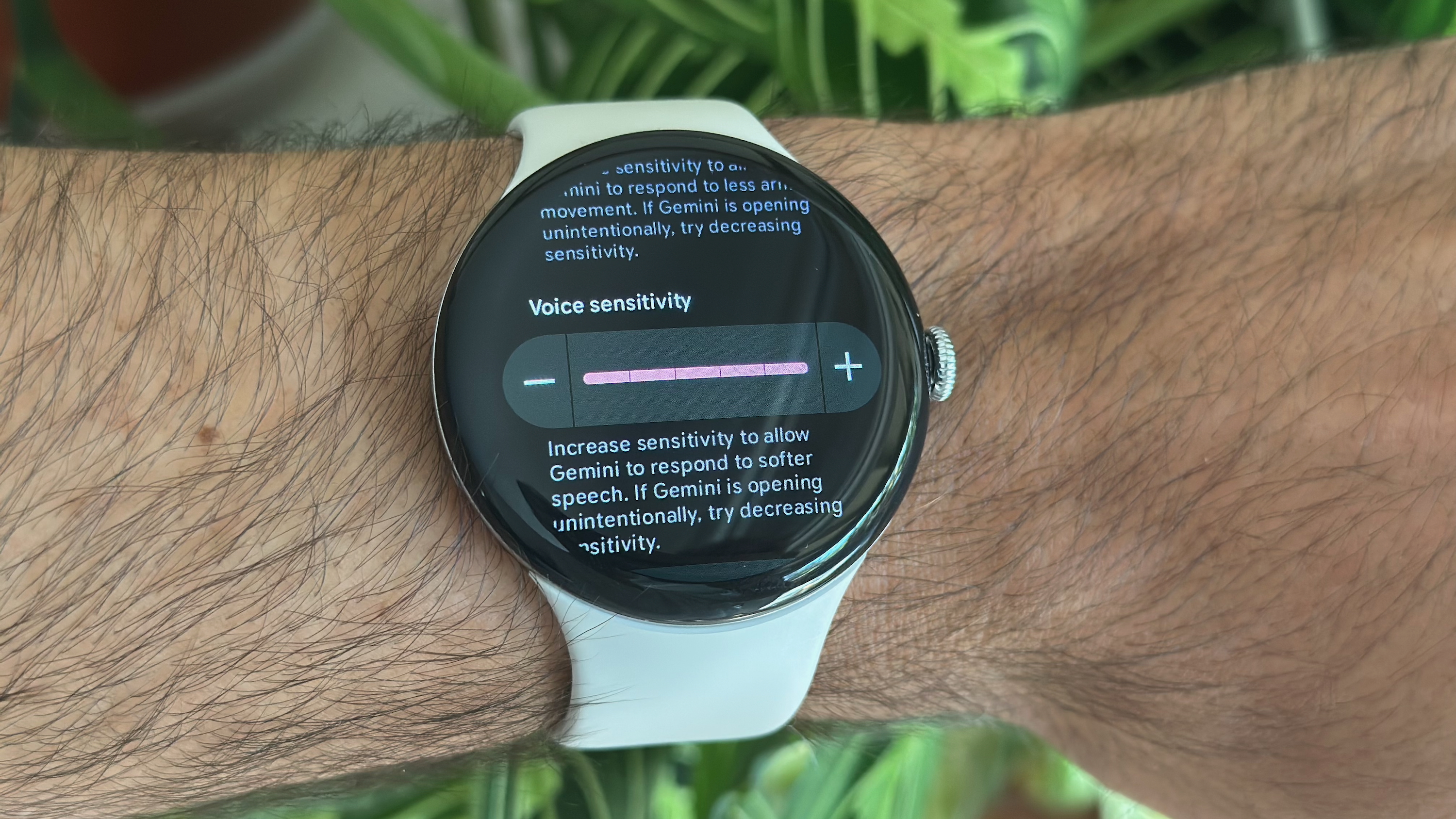 A photo of the Google Pixel Watch 4 on a man&#039;s wrist, showing the Voice sensitivity setting set to 5/5 for the Gemini Raise to Talk feature.