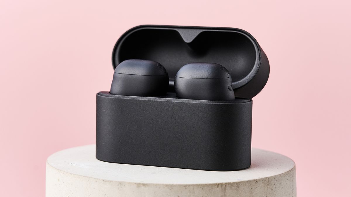 The Sony WF-1000XM6 in their case on top of a stone cylinder in front of a pink background.
