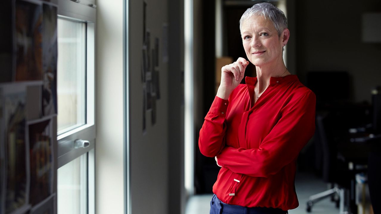 A woman with gray hair thinks intently in an office setting.