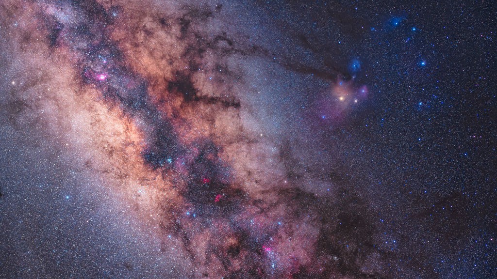 um rico aglomerado de estrelas se espalha pelo céu enquanto a Via Láctea preenche a imagem, à direita está uma estrela vermelha brilhante Antares e a constelação de Escorpião