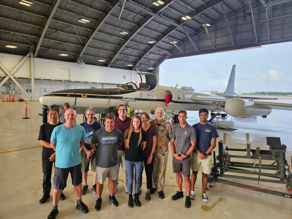 a large group of people stand in a hangar in front of an aircraft