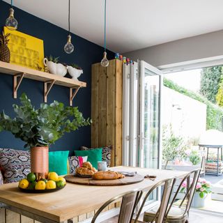 Blue dining room with table, chairs and bench below row of exposed bulbs