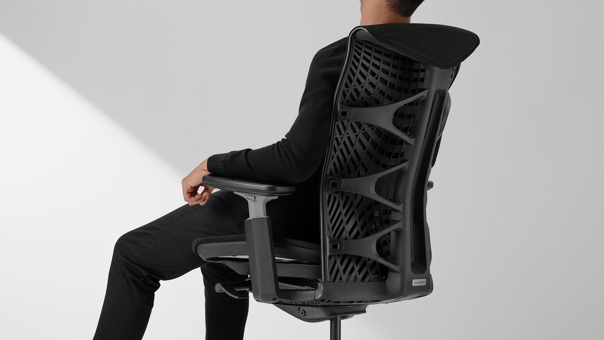 A person sits in a black Autonomous ErgoChair Ultra 2, showcasing its distinctive thermoplastic elastomer (TPE) backrest with a complex, web-like geometric pattern designed for ergonomic support.