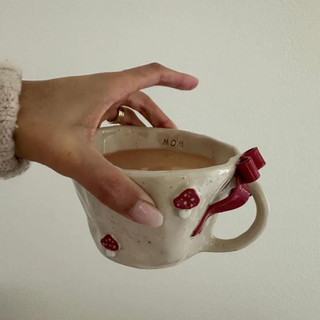 A hand holding a white mug from the top. The mug has 