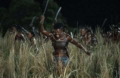 Black woman surrounded by other Black women all holding machetes over their heads running through a field of tall grass at night