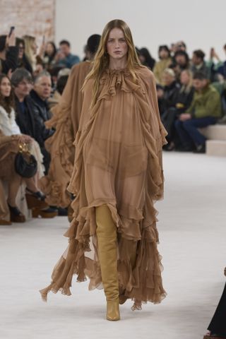 A model at the Chloé fall/winter 2024 runway show wearing a sheer ruffled maxi dress with thigh-high boots.