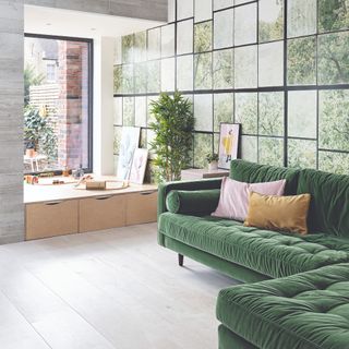 A family living room with a green velvet corner sofa and a play corner for children by a large window