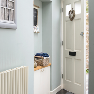 Pale green, grey hallway, white front door, heart shaped reef, alcove with storage unit, framed photo montage.