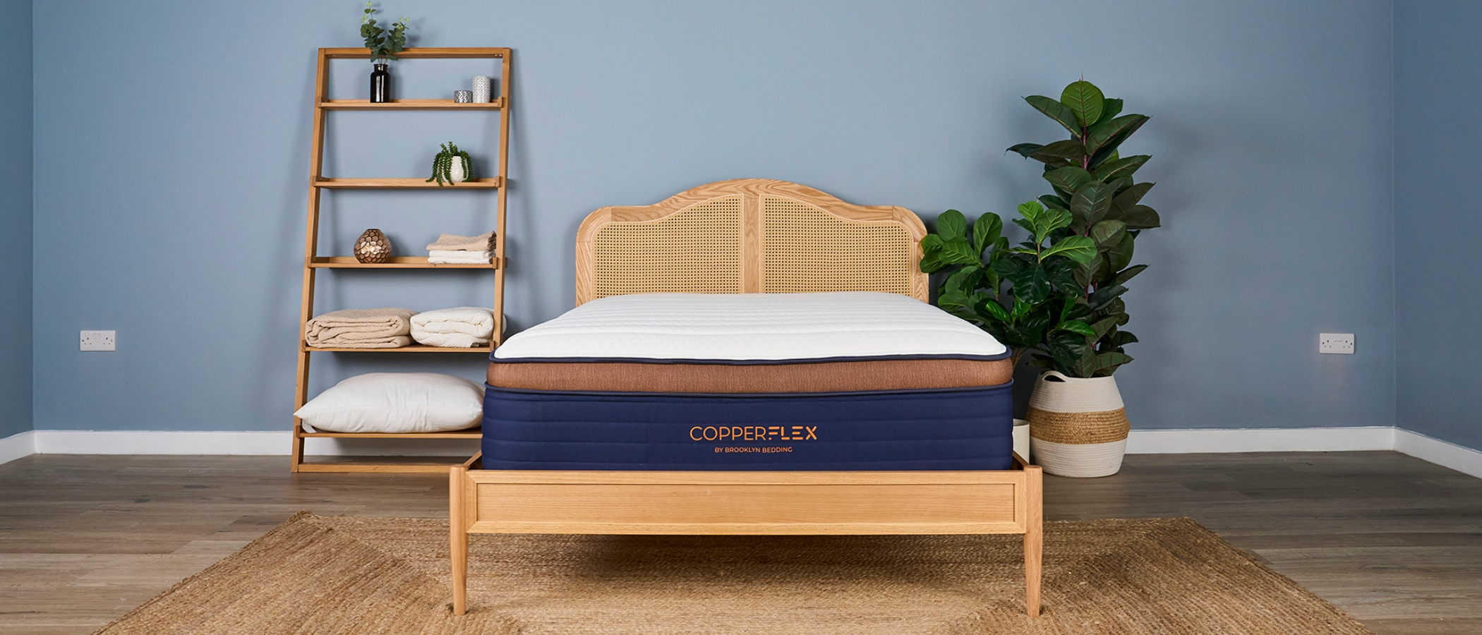 White, navy and bronze Brooklyn Bedding CopperFlex Pro Hybrid Mattress on rattan bedframe in sleep studio with shelves and plants
