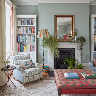 A grey-painted living room with a printed armchair, a checked red ottoman and a floor lamp with a striped lampshade