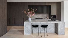 A dark wood kitchen with light wood floor and concrete effect island with black bar stools