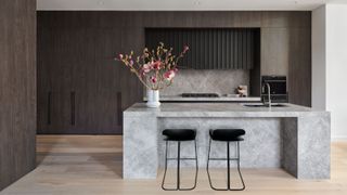 A dark wood kitchen with light wood floor and concrete effect island with black bar stools