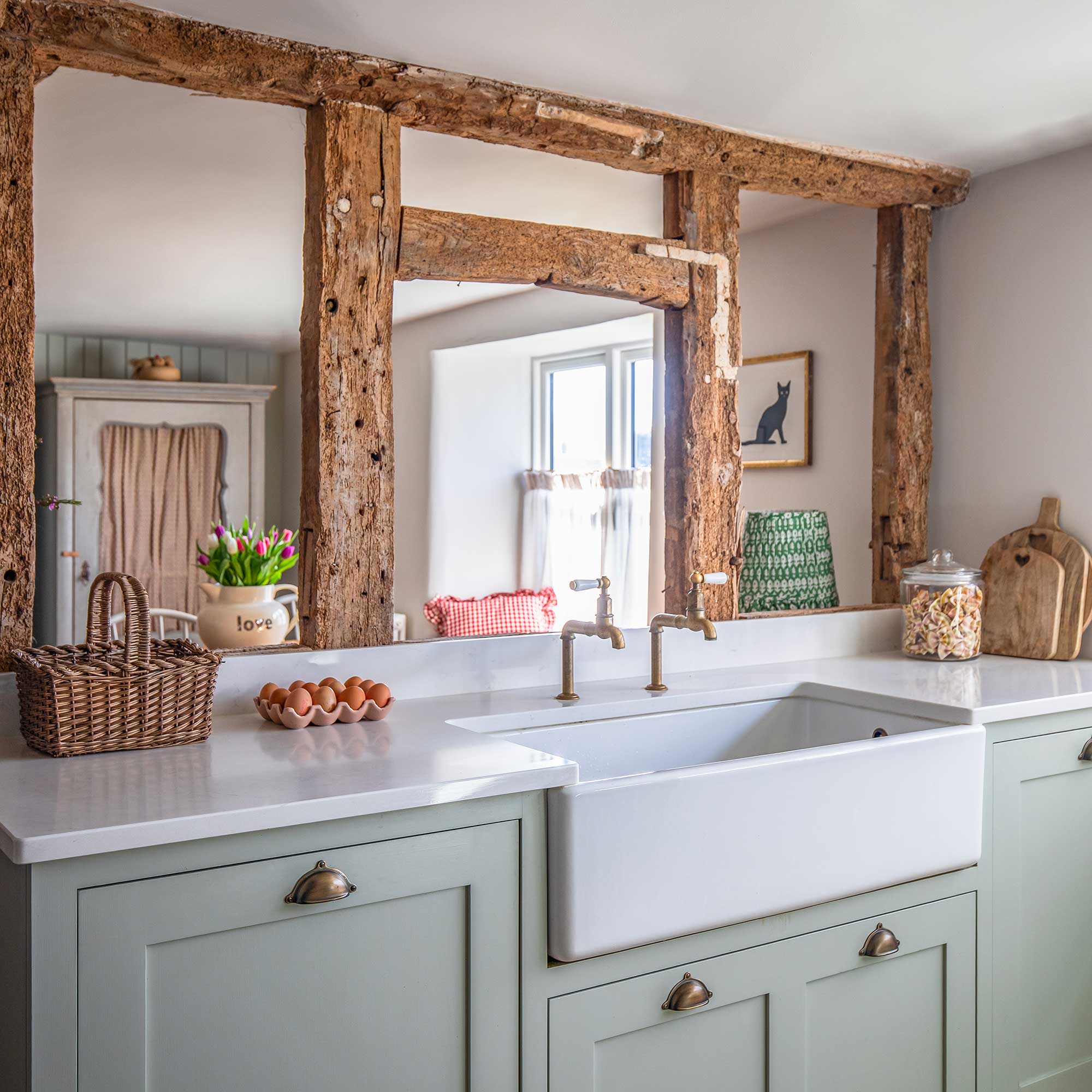 Butlers sink in a run of green kitchen cabinetry with beam wall behind