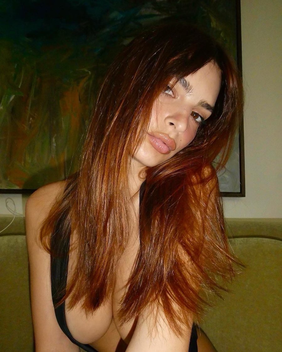 A model, Emily Ratajkowski, takes a selfie in front of a painting with reddish dyed hair.